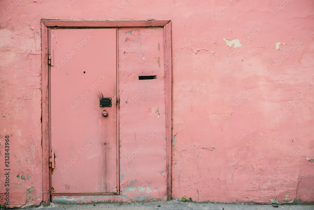 Old pink door with combination lock on unideal peeling wall of aged building. Retro background of entrance in vintage house. Unusual imperfect rough construction. Habitable grunge glamour home.