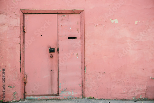 Old pink door with combination lock on unideal peeling wall of aged building. Retro background of entrance in vintage house. Unusual imperfect rough construction. Habitable grunge glamour home. © Daniil