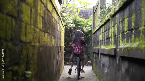 Two children bicycling during golden hour in small alley of Ubud Bali photo