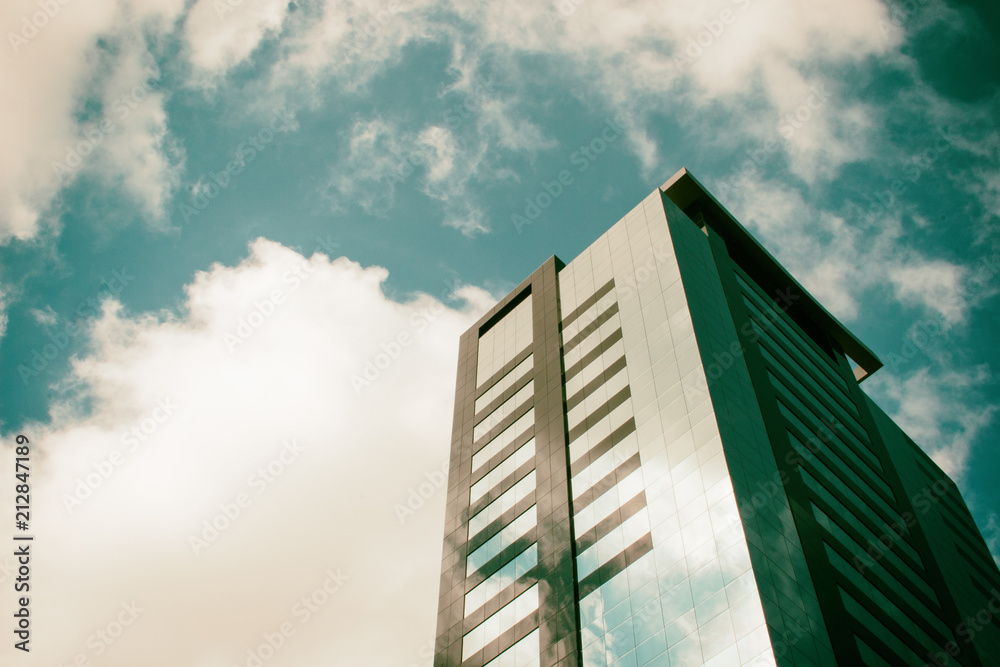 Low angle view of a corporate building with blue sky and clouds in the background surrounded by a golden ambience light.