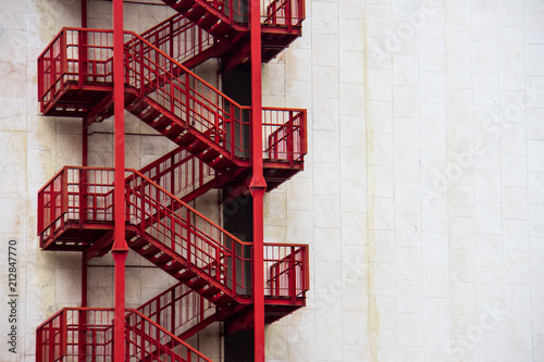 Red external emergency stairs on a white wall of a business building in downtown.