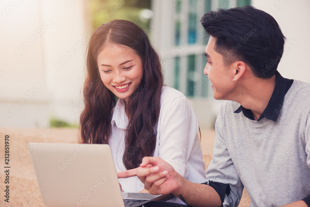 Asian couples students or colleagues sitting at the stairs and smiling as they use laptop computer at campus,Students and education concept Asian couples students or colleagues sitting at the stairs and smiling as they use laptop computer at campus,Students and education concept