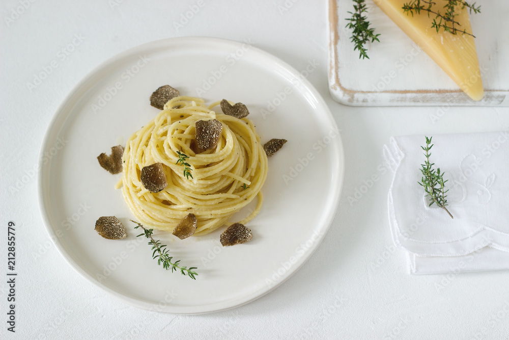 Pasta with creamy cheese sauce and truffle on a light plate, served with cheese and wine.
