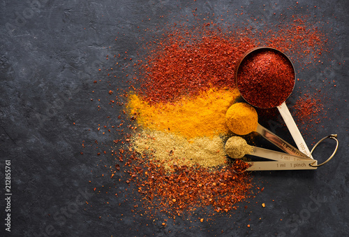 Spices and herbs in measuring spoons on a black background, top view