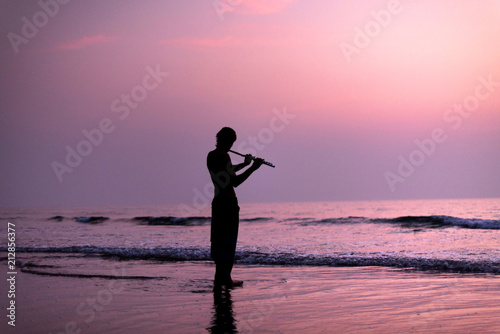 A man is practicing playing the flute on the birch in the sunset. GOA, India. 16.01.2018