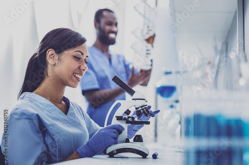 Young chemist. Professional young chemist feeling very inspired while using microscope sitting in modern laboratory