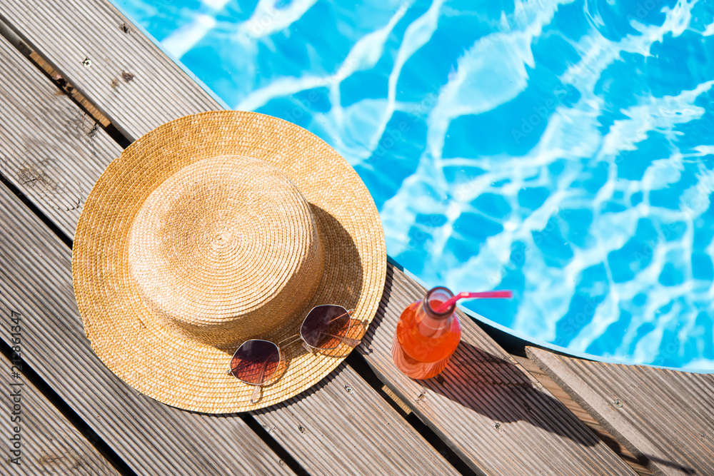 top view of wicker hat, sunglasses and bottle with summer drink near  swimming pool Stock Photo
