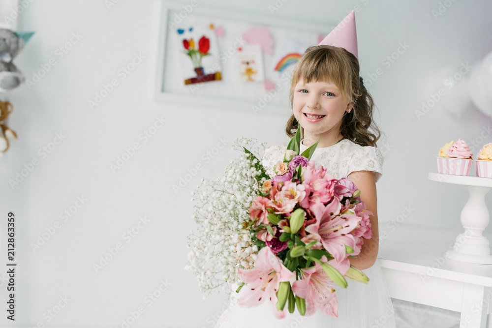 smiling birthday kid in cone holding bouquet of lilies smiling birthday kid in cone holding bouquet of lilies
