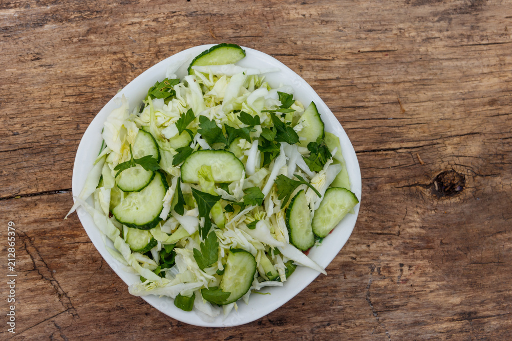 Spring vegan salad with cabbage, cucumber, green onion and parsley on wooden table. Top view Spring vegan salad with cabbage, cucumber, green onion and parsley on wooden table. Top view