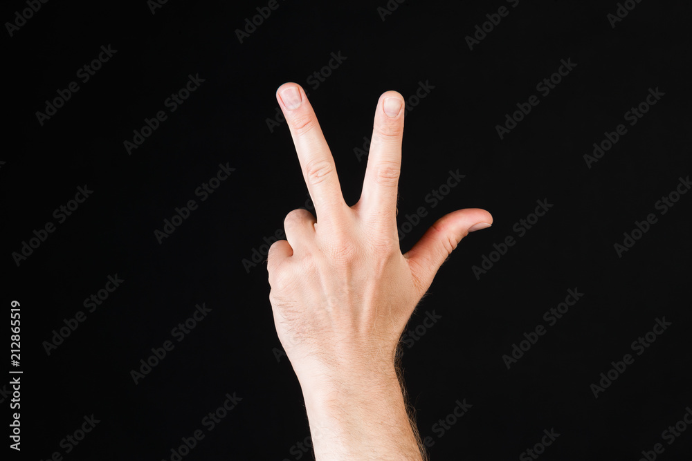Male Caucasian hand showing three fingers in front of black background Male Caucasian hand showing three fingers in front of black background