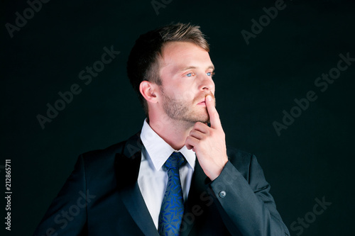 Business man or manager in suit thinking concentrated in front of black background