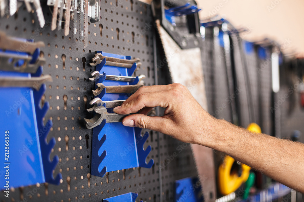 Obraz premium Close up man hand choosing wrenches in workshop isolated