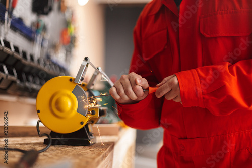 Close up foreman in orange work clothes using knife sharpener in workshop isolated