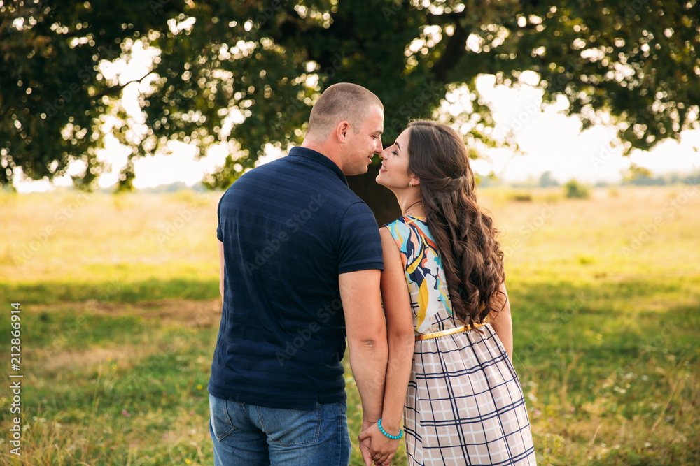 Handsome guy and an attractive girl kiss each other near a large green tree. Love story Handsome guy and an attractive girl kiss each other near a large green tree. Love story