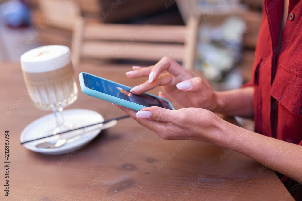 Phone in hands. Elegant appealing woman holding her smart phone in hands while searching info in the Internet Phone in hands. Elegant appealing woman holding her smart phone in hands while searching info in the Internet
