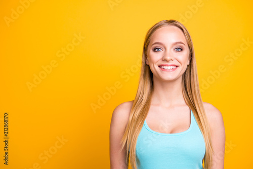 Portrait of young beautiful blond girl, isolated on yellow background with copy space for text. Cute female model with big smile looking at camera