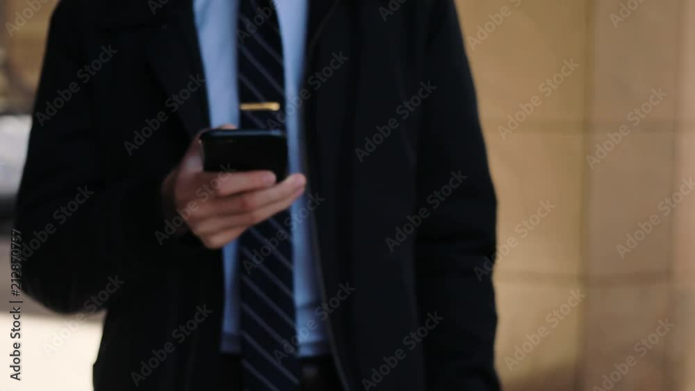 Caucasian guy in shirt and tie walking fast in the street. Young Caucasian man holding cellphone in hands, chatting. City vibes. Outdoors. Caucasian guy in shirt and tie walking fast in the street. Young Caucasian man holding cellphone in hands, chatting. City vibes. Outdoors.