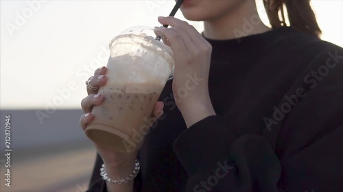 Close up shot of a stylish girl in black clothes drinking sweet cocktail on the beach in summer. Enjoying fresh desert cocktail. Beautiful brunette. photo