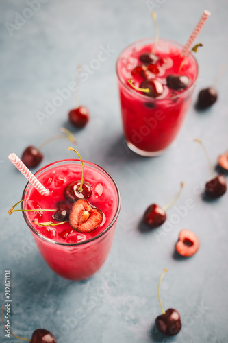 Tasty fresh summer drink cocktail with cherries, coconut milk, juice and ice on blue table background. View from above