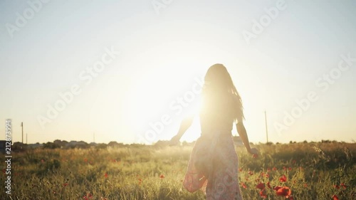 Gorgeous Ukrainian beauty running through field full of red flowers. Attractive Caucasian girl in pink dress in the evening. Countryside. Summertime. Sunset. Outdoors.
