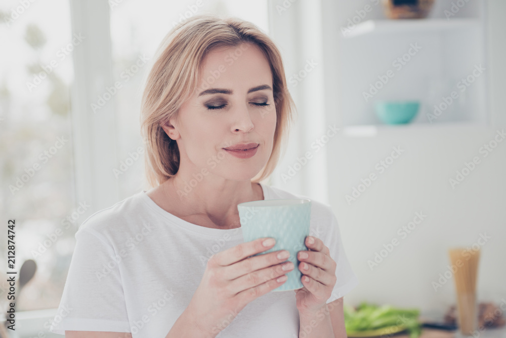 Close up portrait of adorable cheerful smiling young woman with nice manicure keeping glass cup of drink in hands with closed eyes wearing white t-shirt Close up portrait of adorable cheerful smiling young woman with nice manicure keeping glass cup of drink in hands with closed eyes wearing white t-shirt