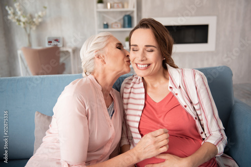 Broad smile. Appealing dark-haired pregnant woman feeling amazing smiling broadly while listening to her mother