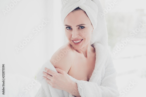 Close up portrait of young attractive adorable cute woman smiling with her teeth wearing bathrobe and turban showing her shoulder looking straight in white interior