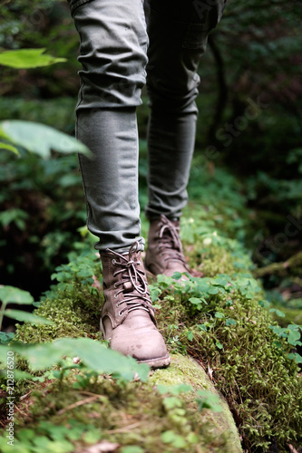Woman's feet in travel boots on a mossy log in the forest. Travel concept.