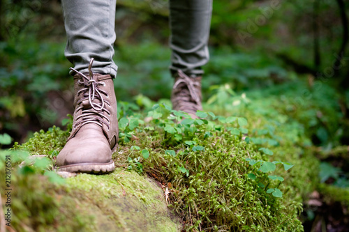 Woman's feet in travel boots on a mossy log in the forest. Travel concept.