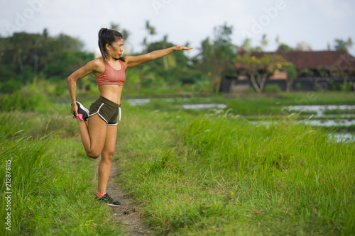 fit and sporty runner Asian woman stretching leg and body after running workout on green field beautiful background in sport training
