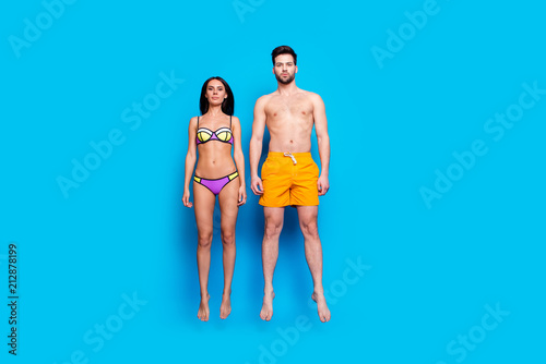Full length portrait of calm young woman and man in swimsuit, jumping and levitating in the air over blue background with copy space for text photo