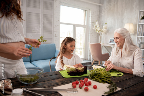 Cooking lunch. Beautiful cute little girl feeling interested while joining her grandmother cooking lunch