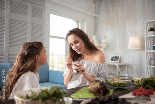Chocolate spread. Pleasant dark-haired pregnant woman eating chocolate spread from spoon with her daughter