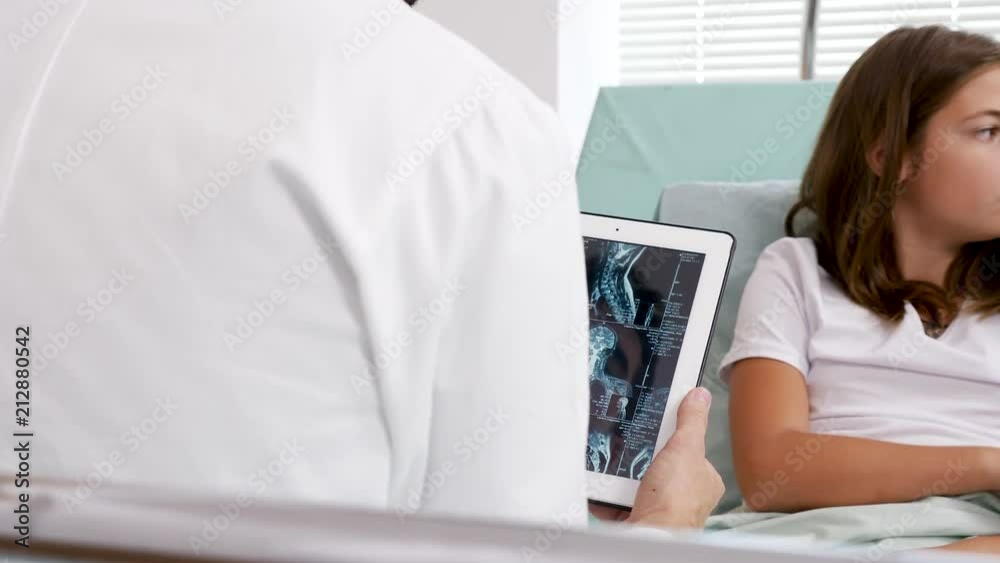 Doctor looking on a digital PC to MRI scan results. The girl patient and her mother are in hospital bed Doctor looking on a digital PC to MRI scan results. The girl patient and her mother are in hospital bed