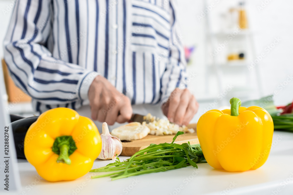cropped image of senior woman cooking in kitchen with bell peppers and green onion on foreground cropped image of senior woman cooking in kitchen with bell peppers and green onion on foreground