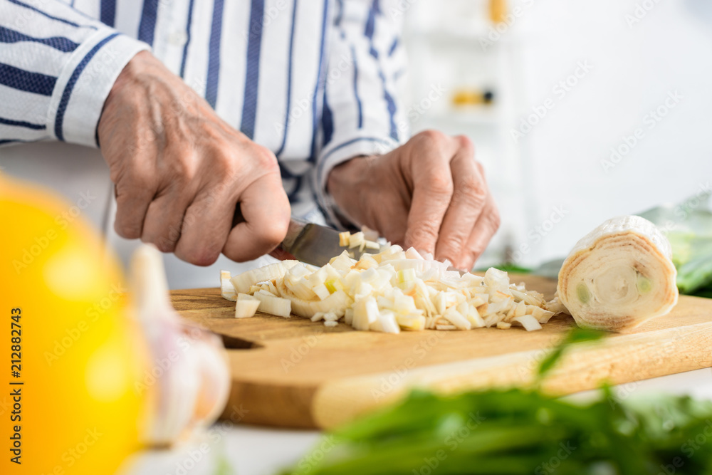 cropped image of grey hair woman cutting leek on wooden board in kitchen cropped image of grey hair woman cutting leek on wooden board in kitchen