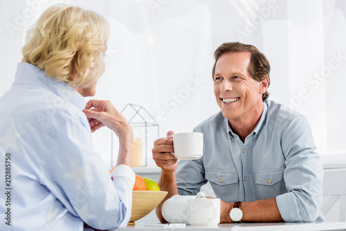 happy elderly couple drinking tea and smiling each other at home