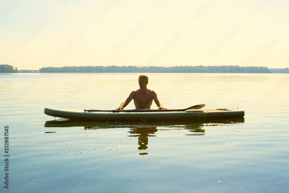 Man is relaxing on a SUP board on a large river