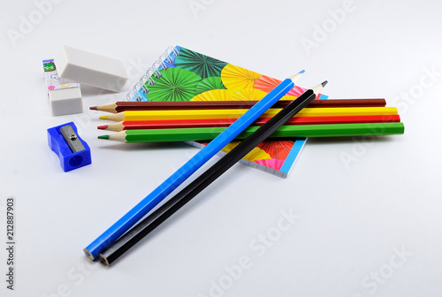 Colorful pencils with erasers, sharpener and note pad on white background.