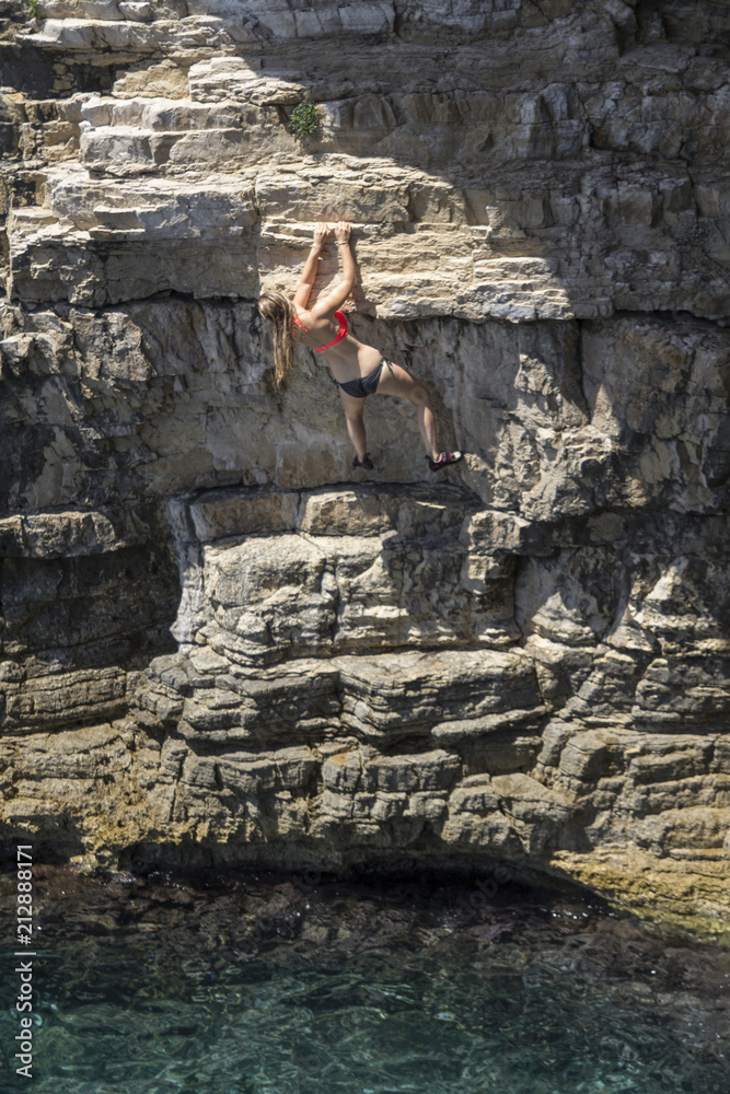 Obraz premium Frau im Bikini klettert an Felswand über dem Wasser
