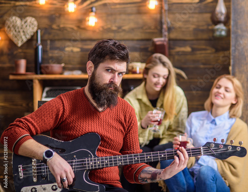 Rock musician with long beard and tattooed arm playing guitar. Bearded man with stern eyes looking at camera. Guitarist composing new song. Man with hipster beard entertaining his wife and daughter