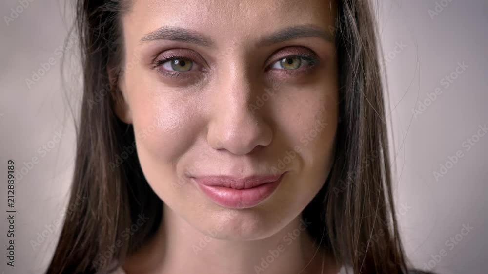 Face of young brunette girl is watching at camera, open eyes, grey background Face of young brunette girl is watching at camera, open eyes, grey background