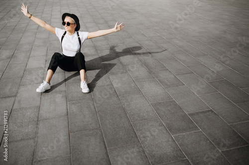 Trendy happy hipster girl with hat and sunglasses have fun sitting on the floor. Copy space area. Freedom concept.