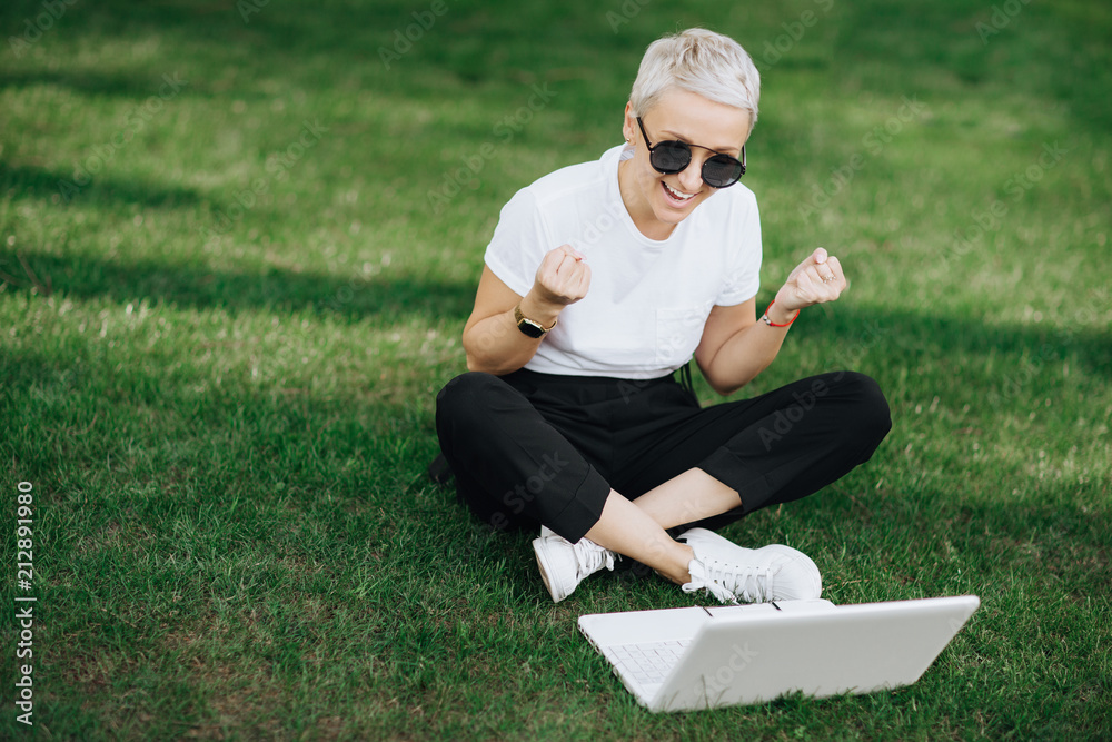 Fototapeta premium Attractive trendy happy hipster young woman with notebook in hat and sunglasses have fun in the park on the grass.