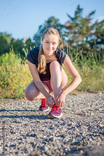 Sport and fitness. Young woman training outdoor is going to tie shoelaces.