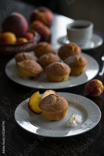 breakfast of homemade muffins with peaches on white plate in dark styled living room photo