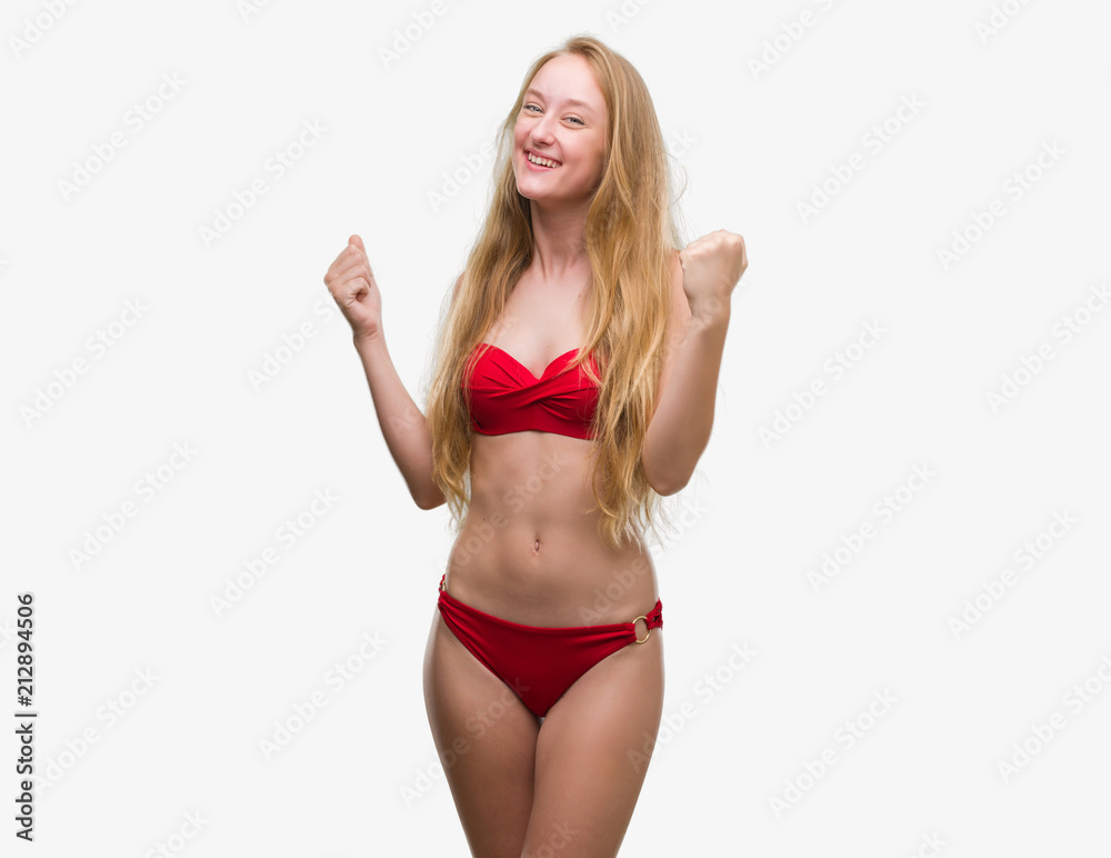 Blonde teenager woman wearing red bikini very happy and excited doing winner gesture with arms raised, smiling and screaming for success. Celebration concept. Blonde teenager woman wearing red bikini very happy and excited doing winner gesture with arms raised, smiling and screaming for success. Celebration concept.