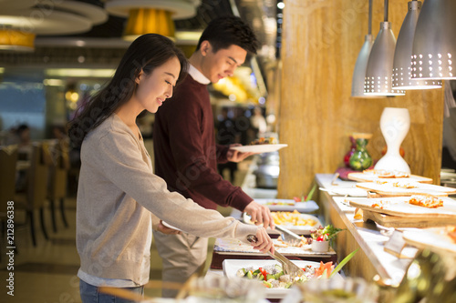 Cheerful young Chinese couple taking food from buffet table photo