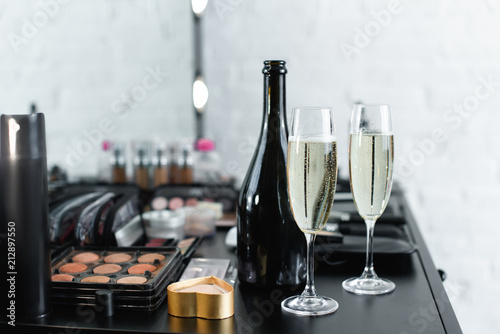 close up view of bottle and glasses of champagne on tabletop with cosmetics for makeup