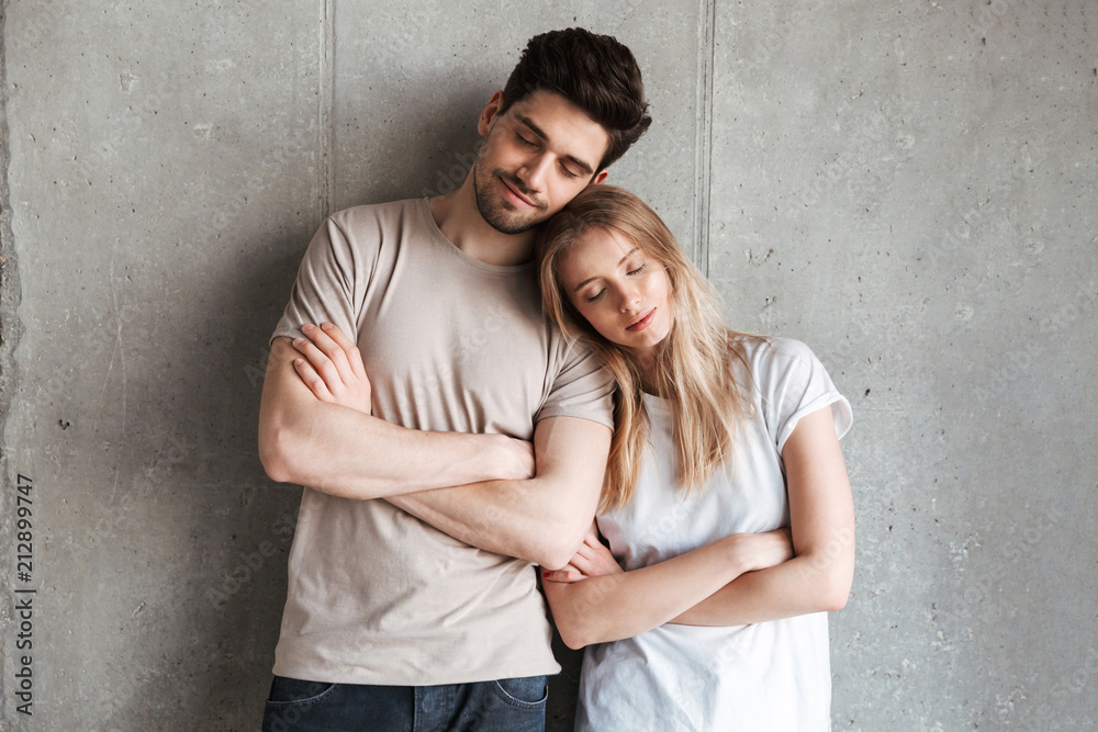 Portrait of attractive european people man and woman in basic clothing standing together with eyes closed and arms crossed, isolated over concrete gray wall indoor